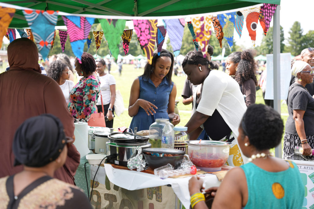 Festival guests are at a food stall. The stallholder is in conversation with a guest.