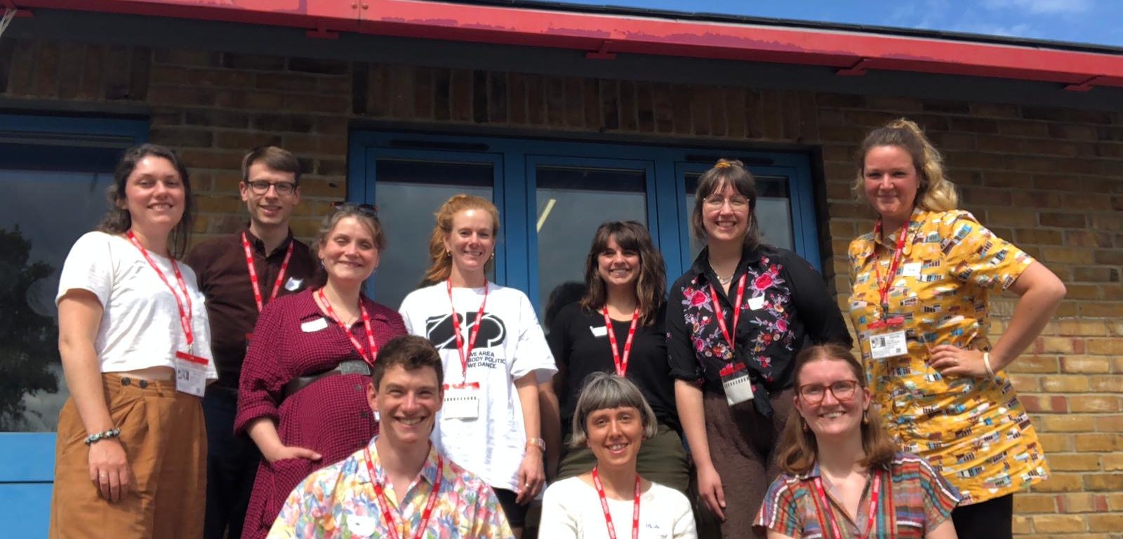 Members of the 'Let's Build a Town' creative team stand together outside. They are smiling and the sky behind them is blue.