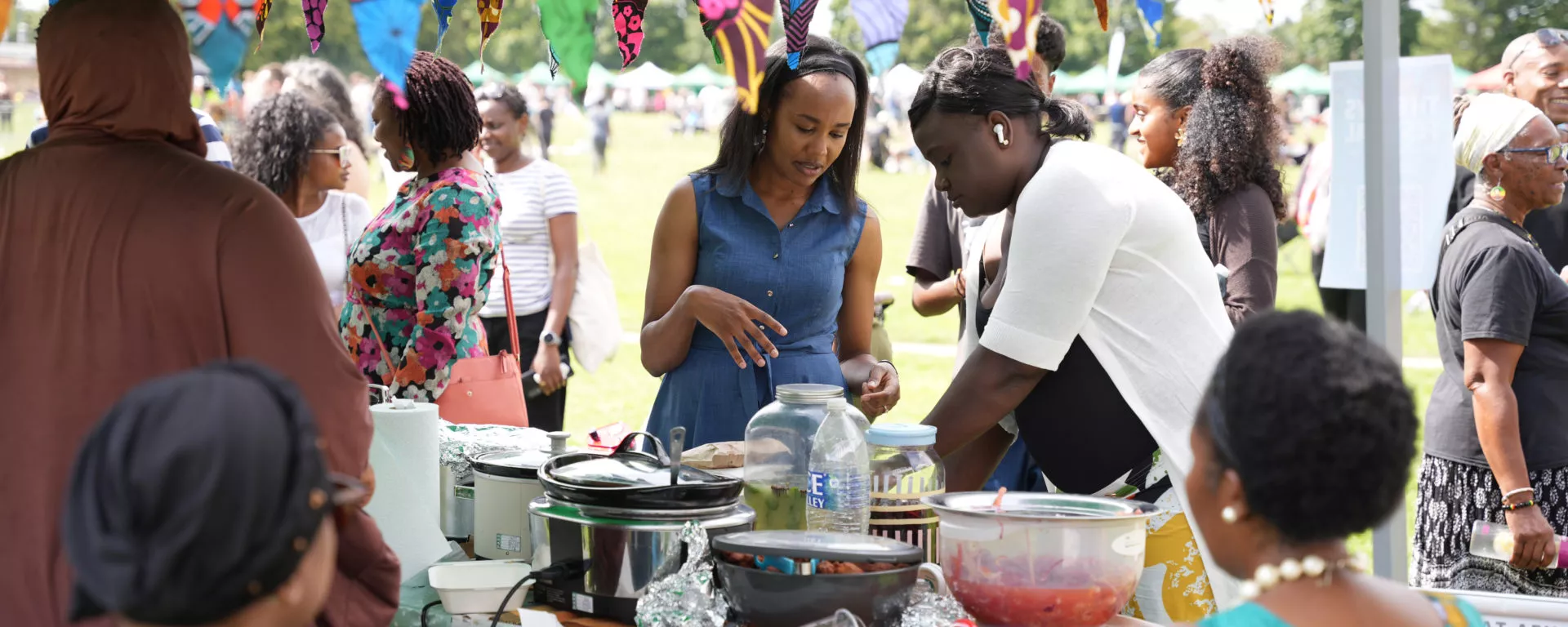 Festival guests are at a food stall. The stallholder is in conversation with a guest.