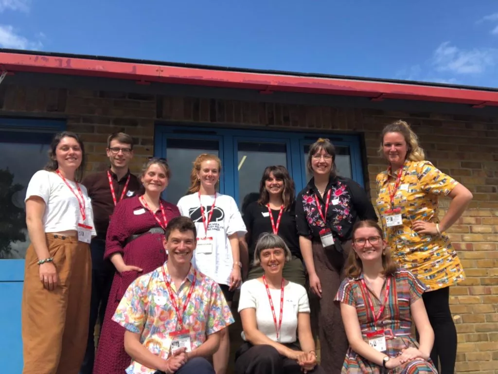 Members of the 'Let's Build a Town' creative team stand together outside. They are smiling and the sky behind them is blue.